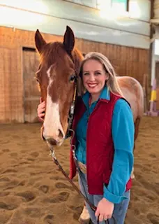 Emily, a kind-hearted barn team member at Barn Owl Venue, standing with her horse inside the indoor riding arena